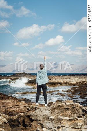 Beautiful girl on the rocky shore of the mediterranean sea relaxes and raises her hand up Beautiful girl on the rocky shore of the mediterranean sea relaxes and raises her hand up 97614282