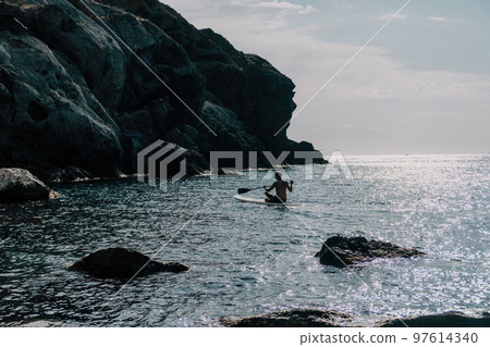 Side view foto of a man swiming and relaxing on the sup board. Sportive man in the sea on the Stand Up Paddle Board SUP. The concept of an active and healthy life in harmony with nature. 97614340