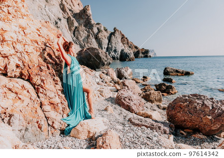 Side view a Young beautiful sensual woman with black hair in a long mint dress posing on a beach with calm sea bokeh lights on sunny day. Girl on the nature on blue sky background. Fashion photo Side view a Young beautiful sensual woman with black hair in a long mint dress posing on a beach with calm sea bokeh lights on sunny day. Girl on the nature on blue sky background. Fashion photo 97614342