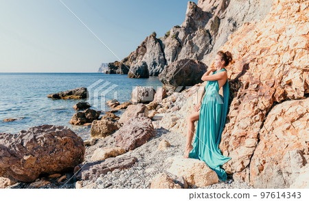 Side view a Young beautiful sensual woman with black hair in a long mint dress posing on a beach with calm sea bokeh lights on sunny day. Girl on the nature on blue sky background. Fashion photo Side view a Young beautiful sensual woman with black hair in a long mint dress posing on a beach with calm sea bokeh lights on sunny day. Girl on the nature on blue sky background. Fashion photo 97614343