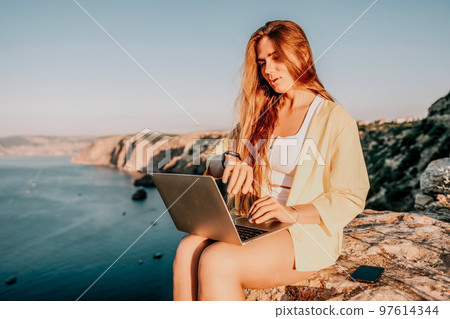 Digital nomad, Business woman working on laptop by the sea. Pretty lady typing on computer by the sea at sunset, makes a business transaction online from a distance. Freelance, remote work on vacation Digital nomad, Business woman working on laptop by the sea. Pretty lady typing on computer by the sea at sunset, makes a business transaction online from a distance. Freelance, remote work on vacation 97614344