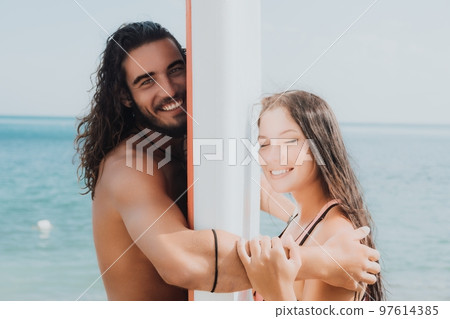 Woman man sea sup. Close up portrait of beautiful young caucasian woman with black hair and freckles looking at camera and smiling. Cute woman portrait in a pink bikini posing on sup board in the sea. 97614385
