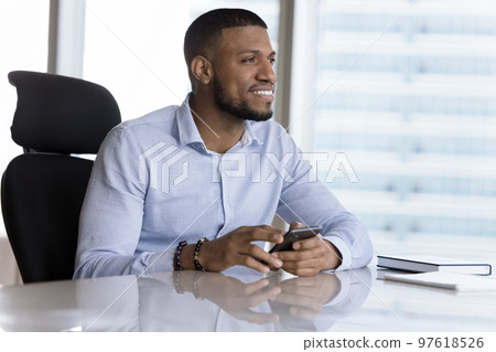 Happy Black business professional man holding cellphone at work table Happy Black business professional man holding cellphone at work table 97618526