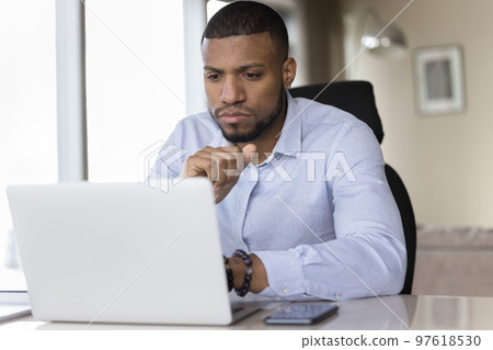 Serious young African business man using Internet app on laptop Serious young African business man using Internet app on laptop 97618530