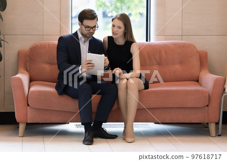 Workmates using digital tablet working seated on sofa in workspace 97618717