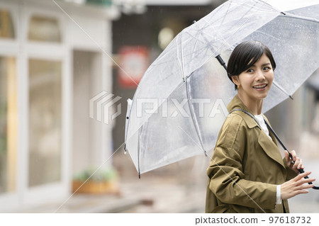 A smiling woman in her early 30s with a plastic umbrella on a rainy day A smiling woman in her early 30s with a plastic umbrella on a rainy day 97618732