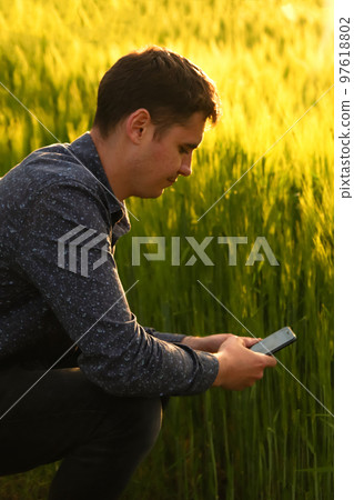 Defocus man with phone on sunset. Young farmer working in a wheat field, inspecting and tuning irrigation center pivot sprinkler system on smartphone. Out of focus 97618802