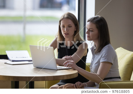 Two women colleagues working together using laptop 97618805
