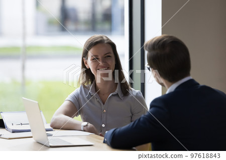 Colleagues communicating seated at desk in modern workspace Colleagues communicating seated at desk in modern workspace 97618843