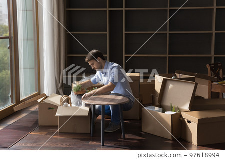 Serious young renter man unpacking stuff, moving into new apartment Serious young renter man unpacking stuff, moving into new apartment 97618994