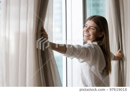 Happy young homeowner, renter woman opening drapes in new apartment Happy young homeowner, renter woman opening drapes in new apartment 97619018