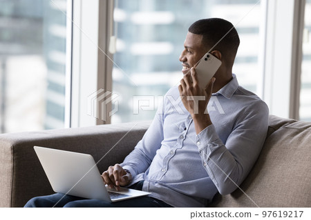 Happy dreamy African digital gadget user man talking on cell Happy dreamy African digital gadget user man talking on cell 97619217