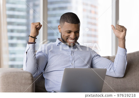 Cheerful happy young millennial Black business man looking at laptop Cheerful happy young millennial Black business man looking at laptop 97619218