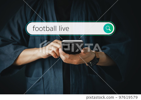 Man using a smartphone in the room for searching football live on internet. Technology concept for mobile phone using search with your website. Man using a smartphone in the room for searching football live on internet. Technology concept for mobile phone using search with your website. 97619579