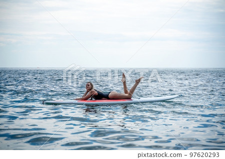 Woman sap sea. Sports girl on a surfboard in the sea on a sunny summer day. In a black bathing suit, he lies on a sap in the sea. Rest on the sea. Woman sap sea. Sports girl on a surfboard in the sea on a sunny summer day. In a black bathing suit, he lies on a sap in the sea. Rest on the sea. 97620293