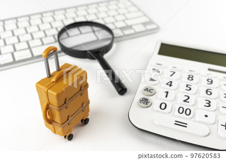 在計算機上預訂旅行的圖像。一個鍵盤,一個手提箱和一個放大鏡。 在計算機上預訂旅行的圖像。一個鍵盤,一個手提箱和一個放大鏡。 97620583