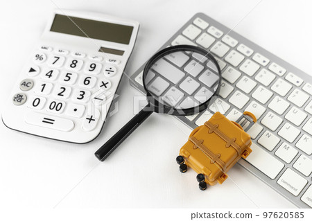 An image of making a reservation for a trip on a computer. A keyboard, a carrying case and a magnifying glass. 97620585