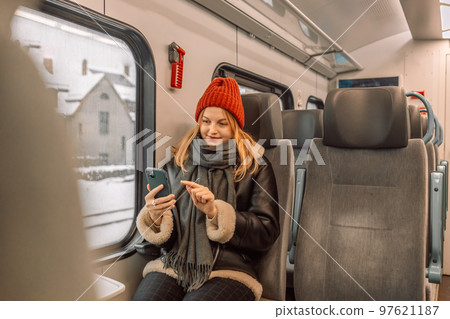 Enjoying travel concept. Young pretty blonde woman tourist traveling by the train sitting near the window using smartphone Enjoying travel concept. Young pretty blonde woman tourist traveling by the train sitting near the window using smartphone 97621187