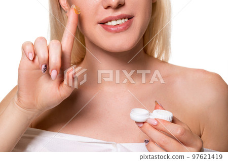Young woman holding contact lenses cases and lens in front of her face on white background 97621419
