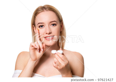 Young woman holding contact lenses cases and lens in front of her face on white background Young woman holding contact lenses cases and lens in front of her face on white background 97621427