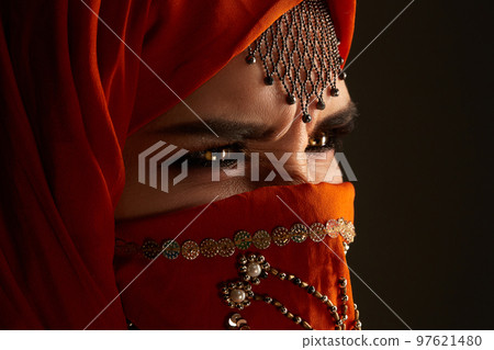 Studio shot of a young charming woman wearing the terracotta hijab decorated with sequins and jewelry. Arabic style. Studio shot of a young charming woman wearing the terracotta hijab decorated with sequins and jewelry. Arabic style. 97621480