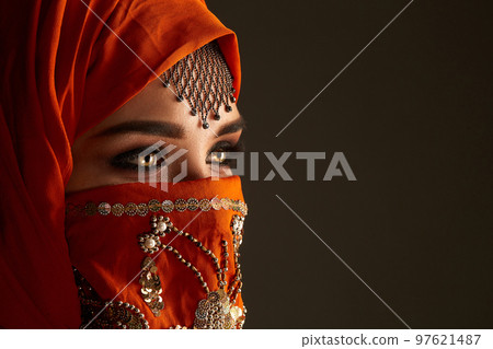 Studio shot of a young charming woman wearing the terracotta hijab decorated with sequins and jewelry. Arabic style. Studio shot of a young charming woman wearing the terracotta hijab decorated with sequins and jewelry. Arabic style. 97621487