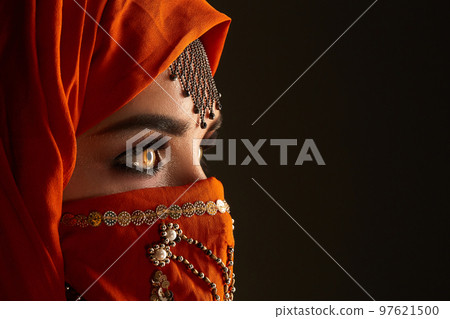 Studio shot of a young charming woman wearing the terracotta hijab decorated with sequins and jewelry. Arabic style. Studio shot of a young charming woman wearing the terracotta hijab decorated with sequins and jewelry. Arabic style. 97621500