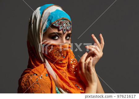 Studio shot of a chrming female wearing the colorful hijab decorated with sequins and jewelry. Arabic style. Studio shot of a chrming female wearing the colorful hijab decorated with sequins and jewelry. Arabic style. 97621617