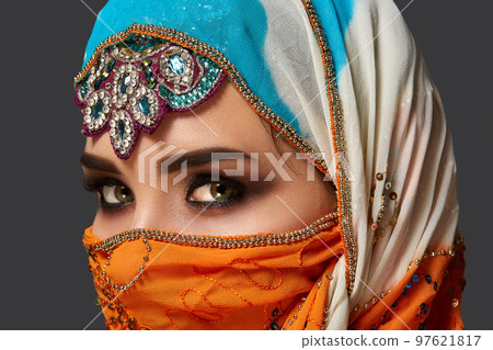 Studio shot of a chrming female wearing the colorful hijab decorated with sequins and jewelry. Arabic style. 97621817