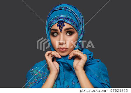 Studio shot of a young beautiful woman wearing the blue hijab decorated with sequins and jewelry. Arabic style. 97621825