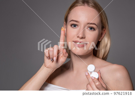 Portrait of young beautiful woman with natural makeup and contact eye lens in hand. Close-up of female model holding white lens box. 97621918