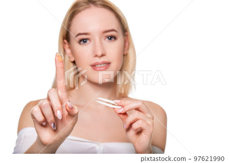 Focus on contact lens on finger of young woman. Young woman holding contact lens on finger in front of her face. Woman holding contact lens on white background. 97621990