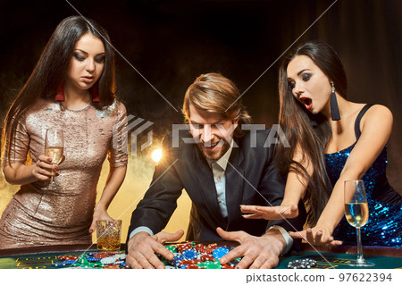 Two beautiful women and young man play on poker table in casino, focus on man and brunette Two beautiful women and young man play on poker table in casino, focus on man and brunette 97622394
