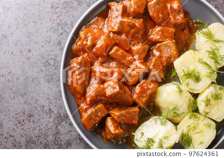 Austrian beef goulash in a thick rich sauce with boiled potatoes close-up in a plate. horizontal top view 97624361