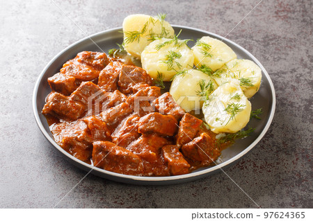 Viennese beef goulash with thick sauce served with boiled potatoes close-up on a plate on the table. horizontal 97624365
