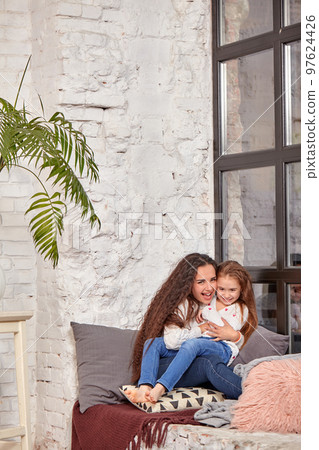 Mother and daughter sitting on sill near window in room Mother and daughter sitting on sill near window in room 97624426