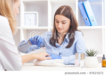 finger nail care by manicure specialist in beauty salon. Manicurist clear cuticle with professional scissors for manicure finger nail care by manicure specialist in beauty salon. Manicurist clear cuticle with professional scissors for manicure 97625872