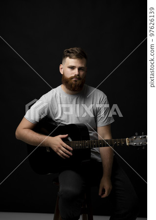 Bearded musician playing acoustic guitar in a dark room. Bearded musician playing acoustic guitar in a dark room. 97626139