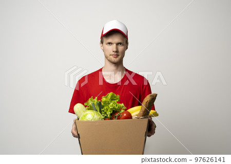 Delivery man in a red uniform holding paper box and delivering food to customer at doorway. Delivery man in a red uniform holding paper box and delivering food to customer at doorway. 97626141