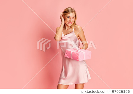 Portrait of beautiful young woman posing in teder silk dress over pink background. Receiving presents. Holidays, celebration and women concept 97626366