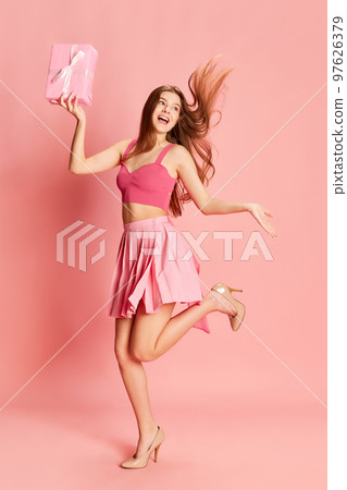 Portrait of beautiful young girl in cute costume posing with present box over pink background. Party gifts 97626379