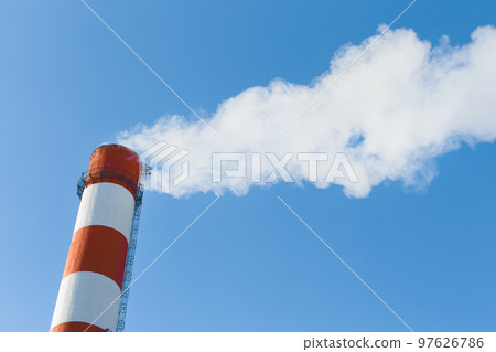 Pollution of the environment, ecology and air. Withdrawal of combustion products of soot, smoke and gases from the pipe of an industrial plant into the atmosphere against the background of a blue sky 97626786