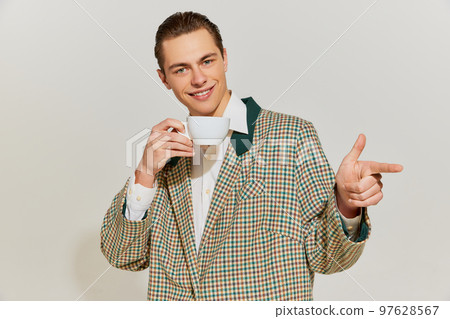 Portrait of young handsome man in vintage costume drinking coffee with seductive smile over grey background. Concept of retro fashion, style, emotions 97628567