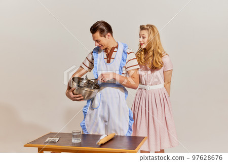 Breaking gender stereotypes. Friendly family couple in retro style clothes cooking at kitchen isolated over light background. Concept of relationship, retro style, creativity, hobbies. Breaking gender stereotypes. Friendly family couple in retro style clothes cooking at kitchen isolated over light background. Concept of relationship, retro style, creativity, hobbies. 97628676