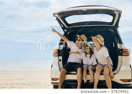 Family Day. Father, Mother and daughter enjoying road trip sitting on back car and point finger out blue sky, Happy people having fun in summer vacation on beach, Family travel in holiday at sea beach 97629461