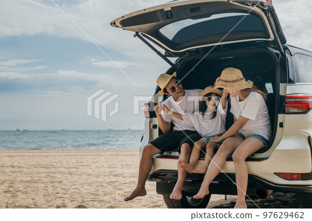 Happy Family Day. Dad, mom and daughter enjoying road trip sitting on back car, Parents and children traveling in holiday at sea beach, family having fun in summer vacation on beach with automobile 97629462