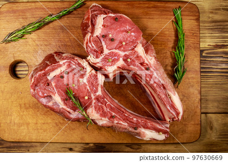 Raw fresh beef rib eye steaks on bone with spices and rosemary on wooden table. Top view 97630669