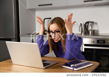 Annoyed young adult woman in glasses work study at kitchen using laptop. Remote education Annoyed young adult woman in glasses work study at kitchen using laptop. Remote education 97632092