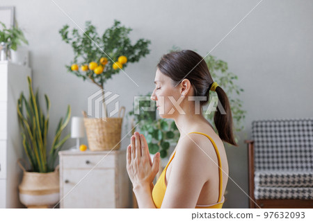 woman in yellow top does yoga and meditation at home on mat. lady is engaged in physical exercises  97632093