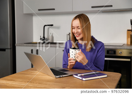 Happy young adult woman work study at kitchen using laptop. Remote education 97632096